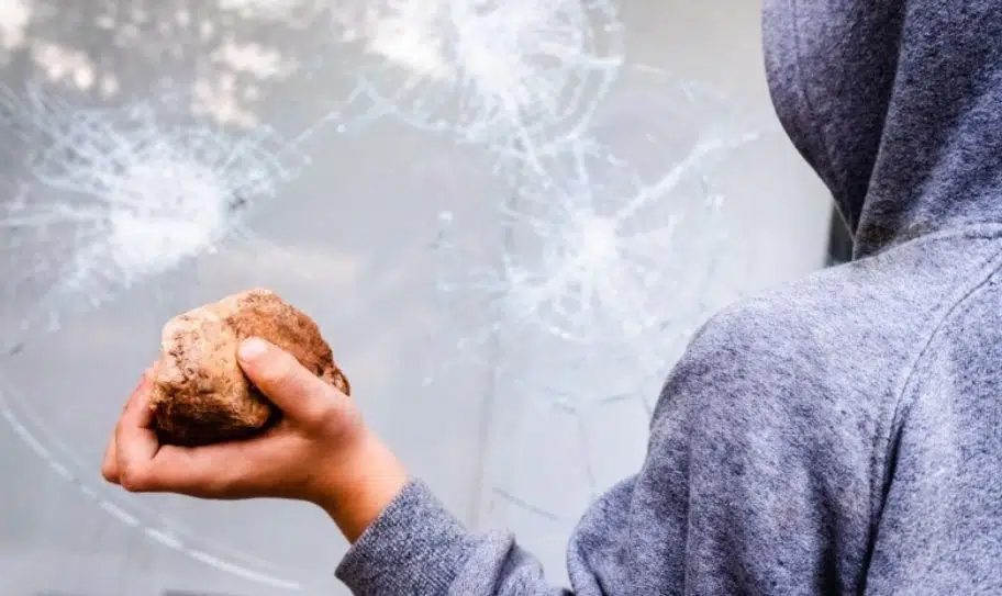 personne avec une pierre à la main devant une vitrine avec film anti-effraction